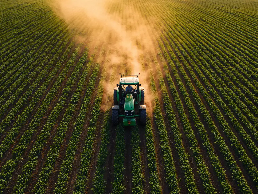 Foto aérea de trator pulverizando uma lavoura ao entardecer